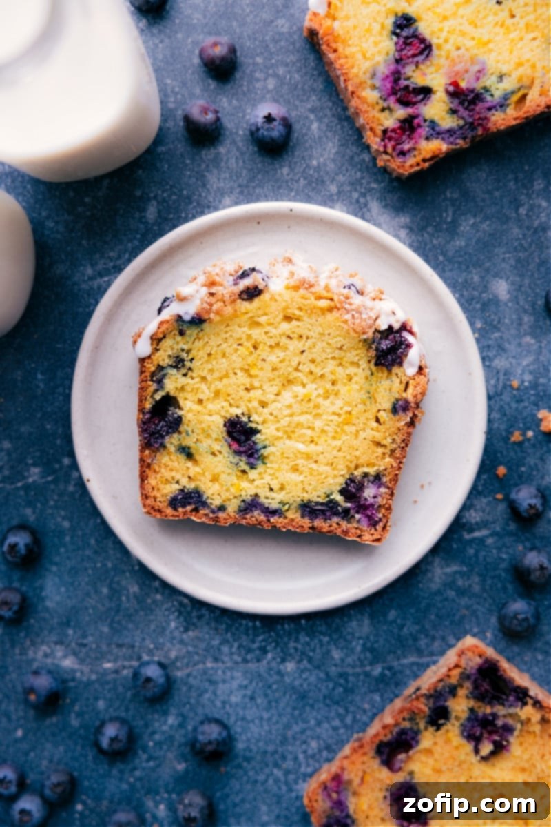 A perfectly baked slice of lemon blueberry bread, revealing its moist and tender interior, generously dotted with blueberries and finished with a sweet lemon icing.