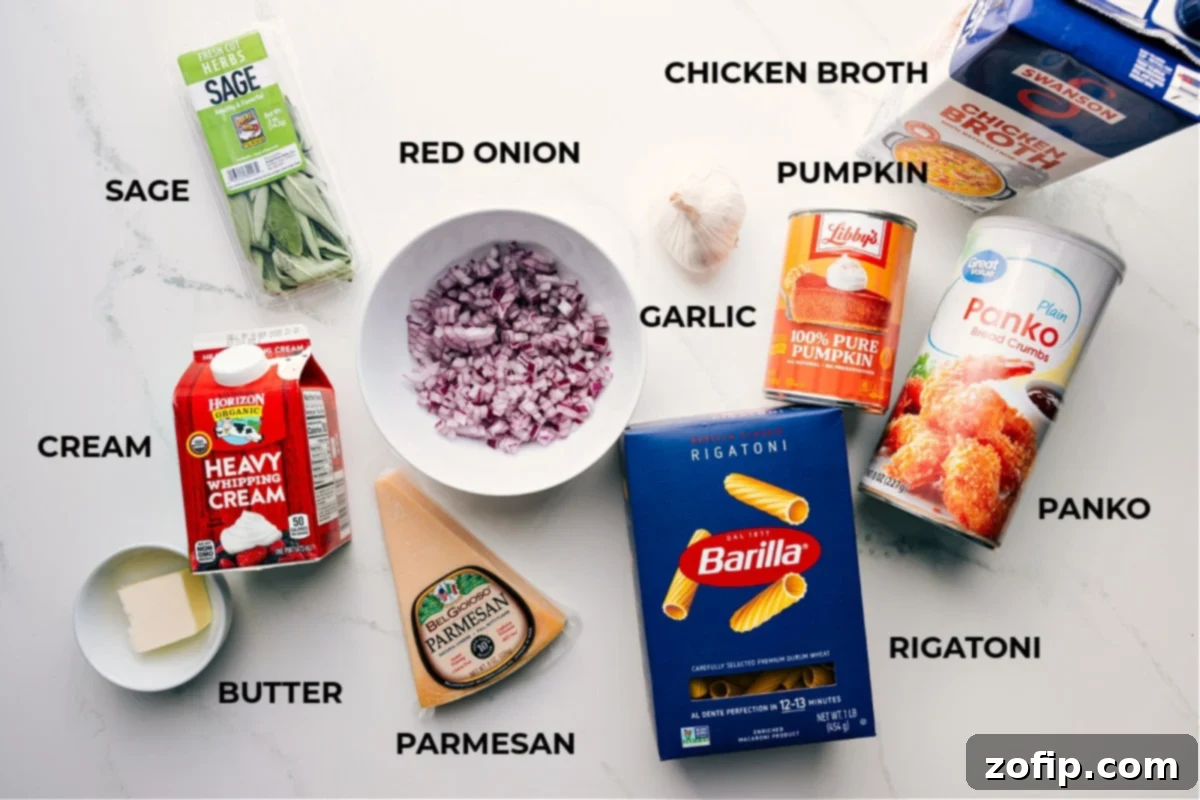 All the essential ingredients for creamy pumpkin pasta, prepped and laid out on a wooden board. Includes butter, cream, Parmesan cheese, fresh sage, red onion, garlic, rigatoni pasta, panko breadcrumbs, canned pumpkin puree, and chicken broth.