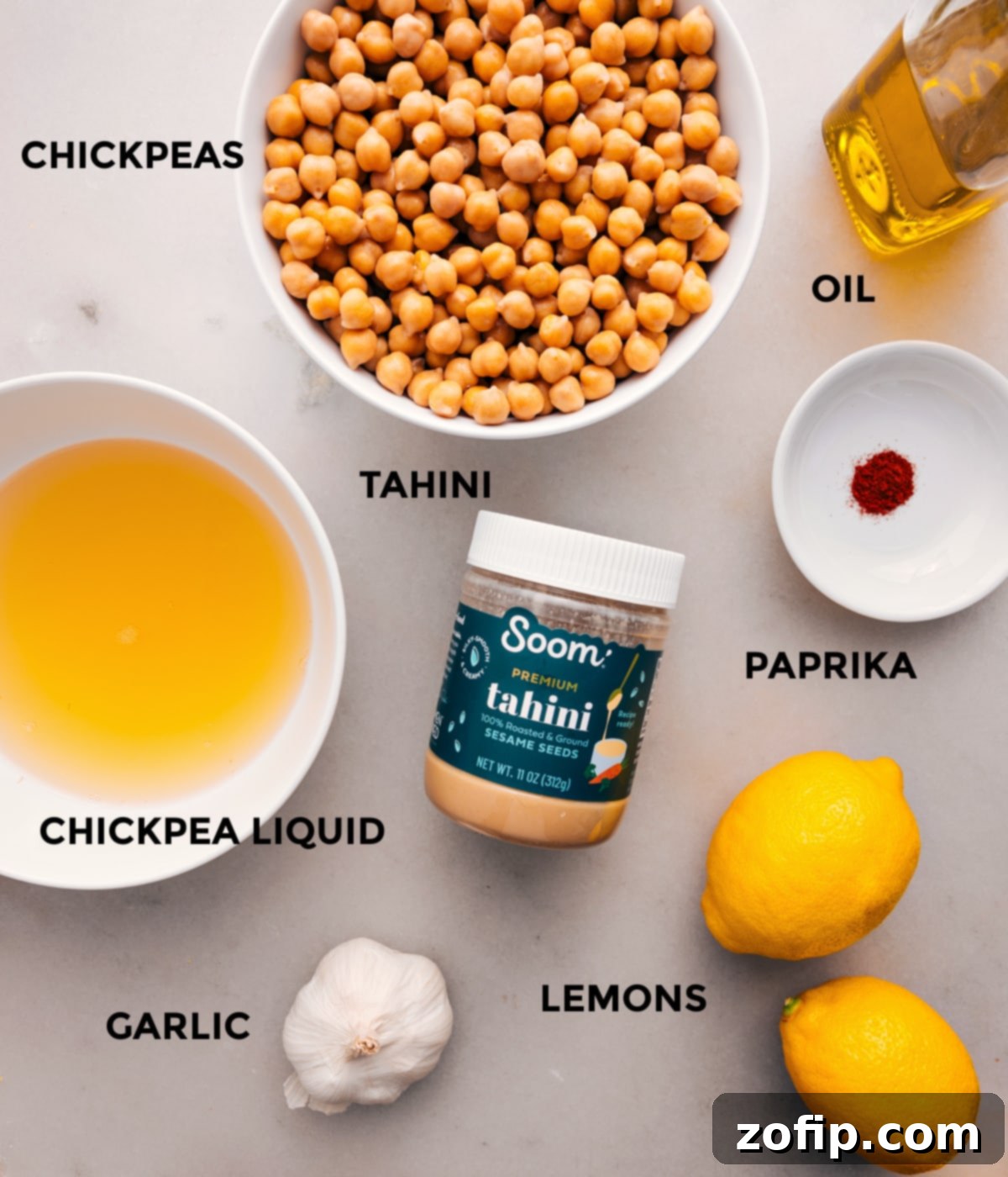 Essential Ingredients for the Best Hummus Recipe A curated display of fresh hummus ingredients including canned chickpeas, olive oil, tahini, whole lemons, garlic cloves, and a sprinkle of paprika, all prepped for blending.
