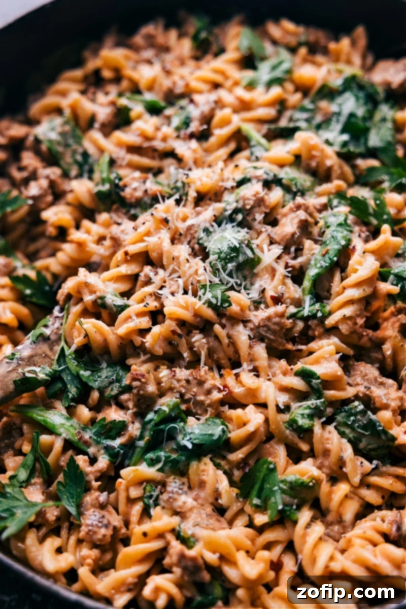 Overhead image of a large bowl of creamy sausage pasta, garnished with fresh parsley and extra Parmesan cheese.