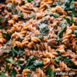 A close-up of the finished creamy sausage pasta dish, showing the sausage, spinach, and sauce-coated rotini pasta.