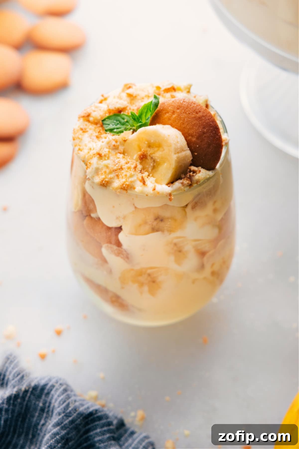 A glass filled with layers of the delicious banana pudding recipe, alternating between creamy pudding, crunchy vanilla cookies, and sliced fresh bananas, crowned with cookie crumbs for a perfect finish.