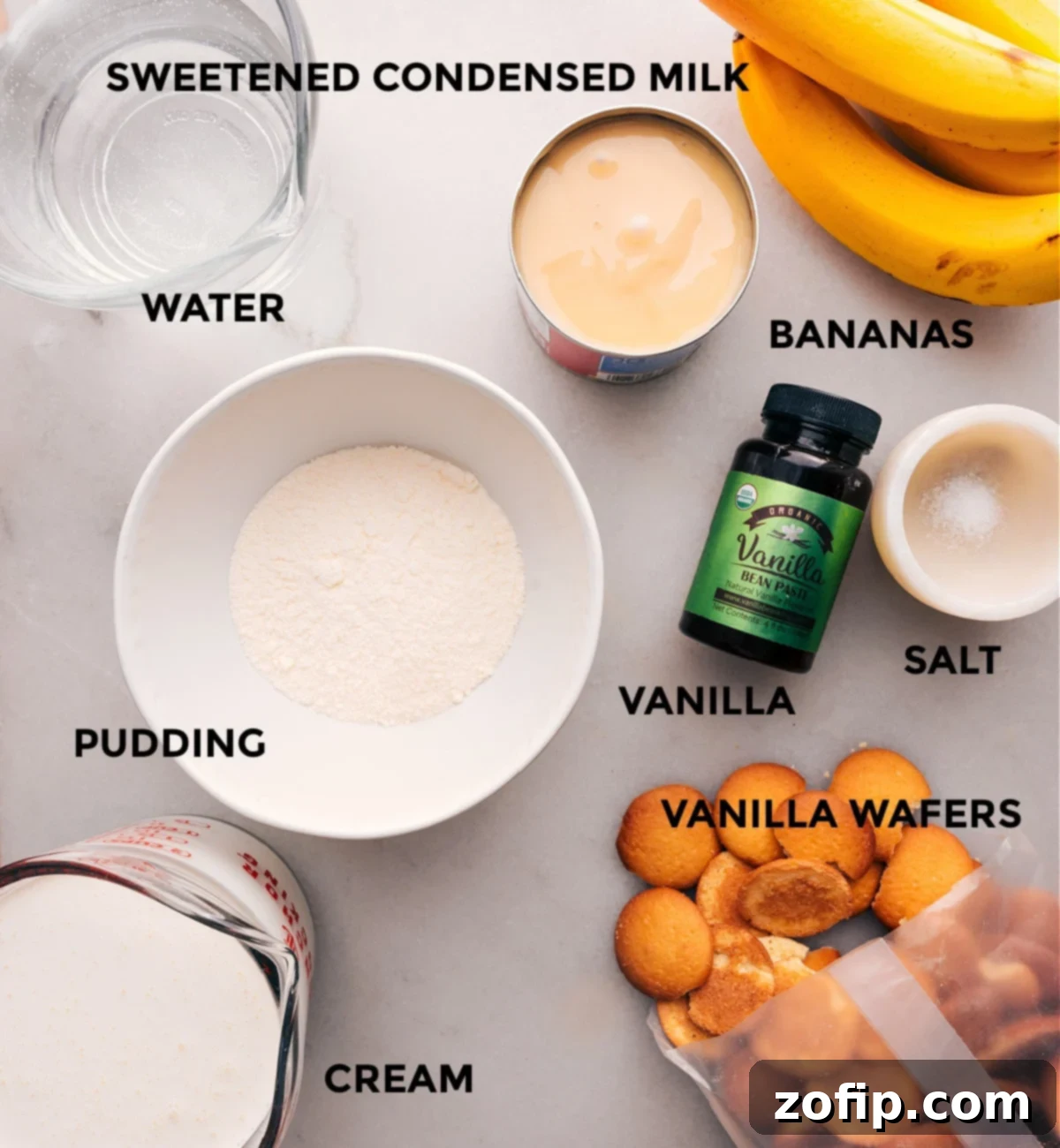 An array of ingredients laid out on a table, including cans of sweetened condensed milk, a box of vanilla wafers, a carton of heavy cream, and vanilla extract, all ready to be transformed into a delicious banana pudding.