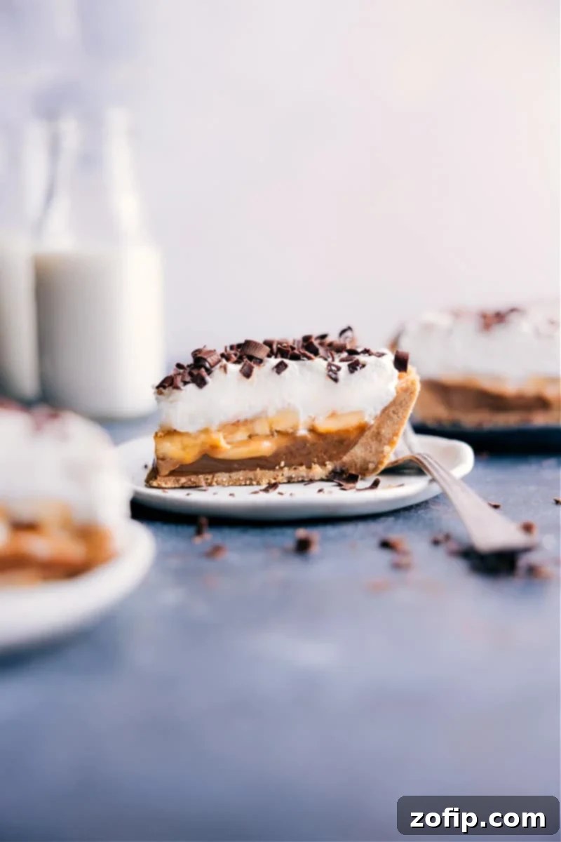 A slice of homemade Banoffee Pie on a white plate, showcasing its layers of golden crust, caramel, bananas, and whipped cream, topped with chocolate shavings.