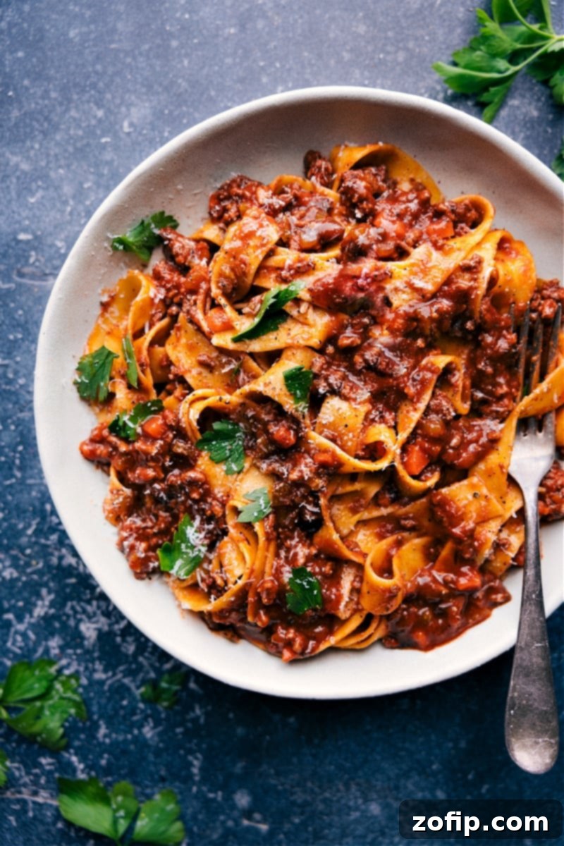 Overhead image of the best Ragu served with pasta, garnished with herbs and Parmesan cheese.