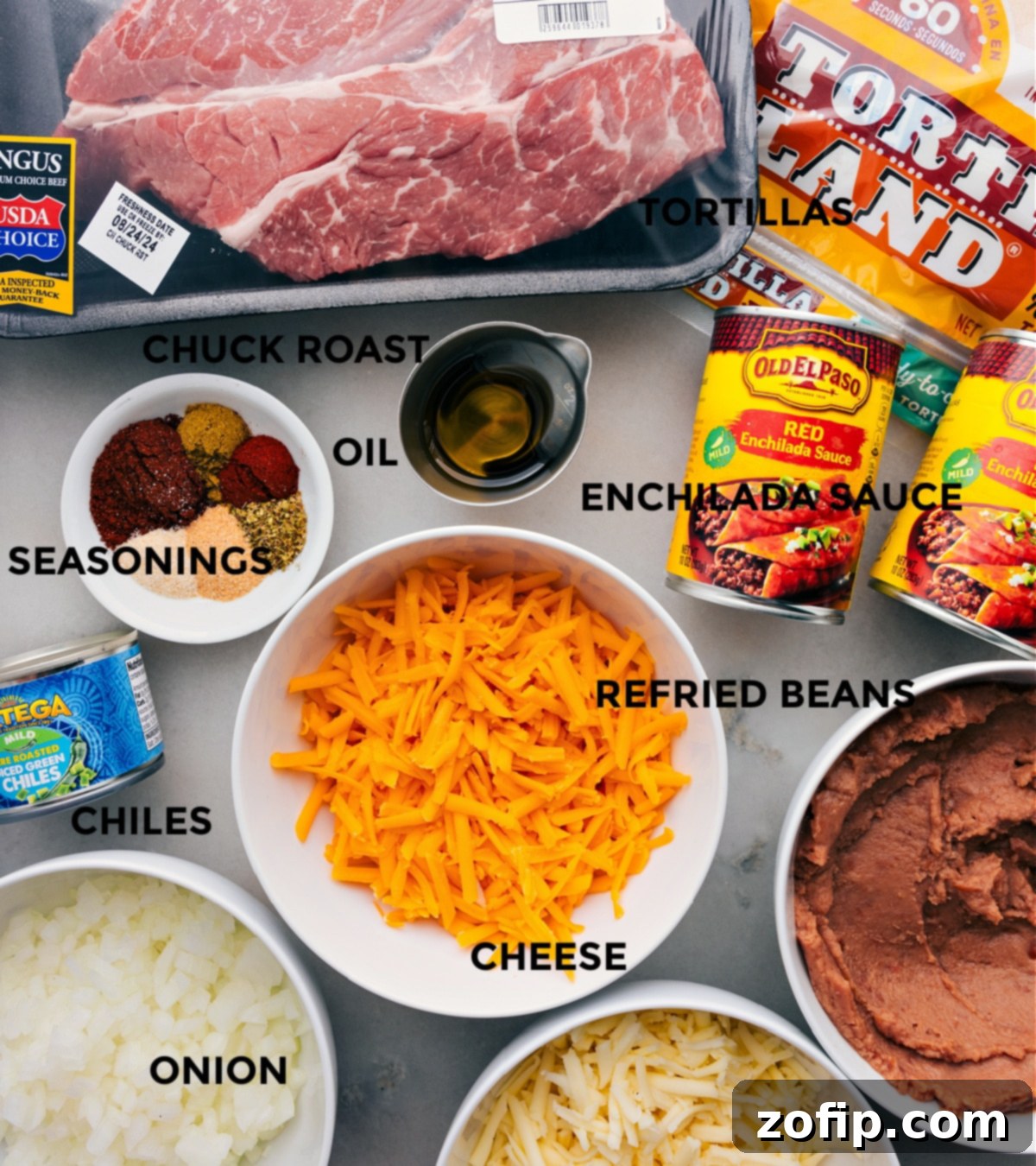 Shredded Beef Enchilada Ingredients Ready To Go All essential ingredients for shredded beef enchiladas laid out and prepped: beef chuck roast, diced yellow onion, olive oil, red enchilada sauce, green chiles, refried beans, flour tortillas, shredded cheddar and Monterey Jack cheeses, and taco seasoning.