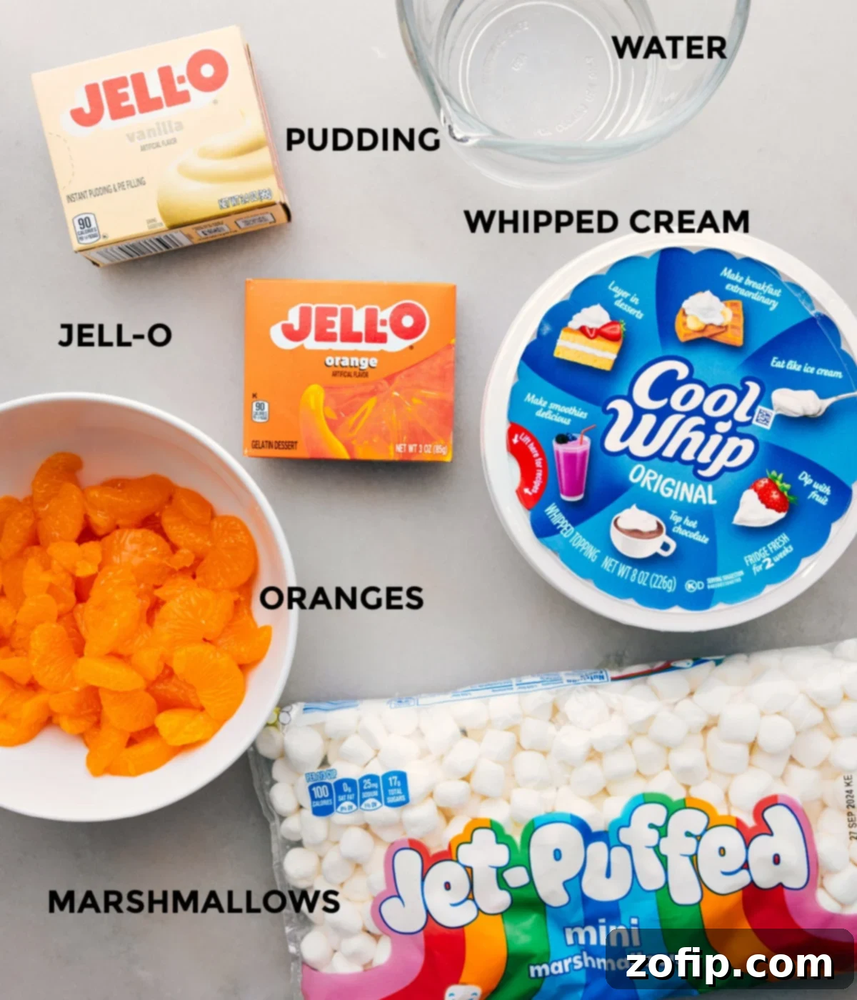 Ingredients In Orange Fluff Salad All the essential ingredients for Orange Fluff Salad neatly prepped and laid out, including mandarin oranges, orange Jell-O mix, vanilla pudding mix, whipped topping, and mini marshmallows, ready for assembly.