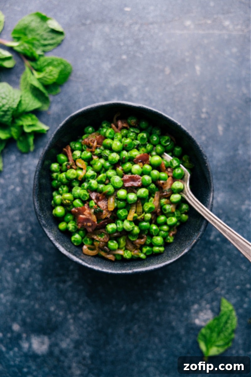 This Frozen Peas recipe is a total show-stopper! With crisp bacon, caramelized shallots, and a touch of garlic! Recipe via chelseasmessyapron #sidedish #best #quick #easy #simple #bacon #frozenpeas #recipe Overhead image of Frozen Peas in a serving bowl, garnished and ready for the table.