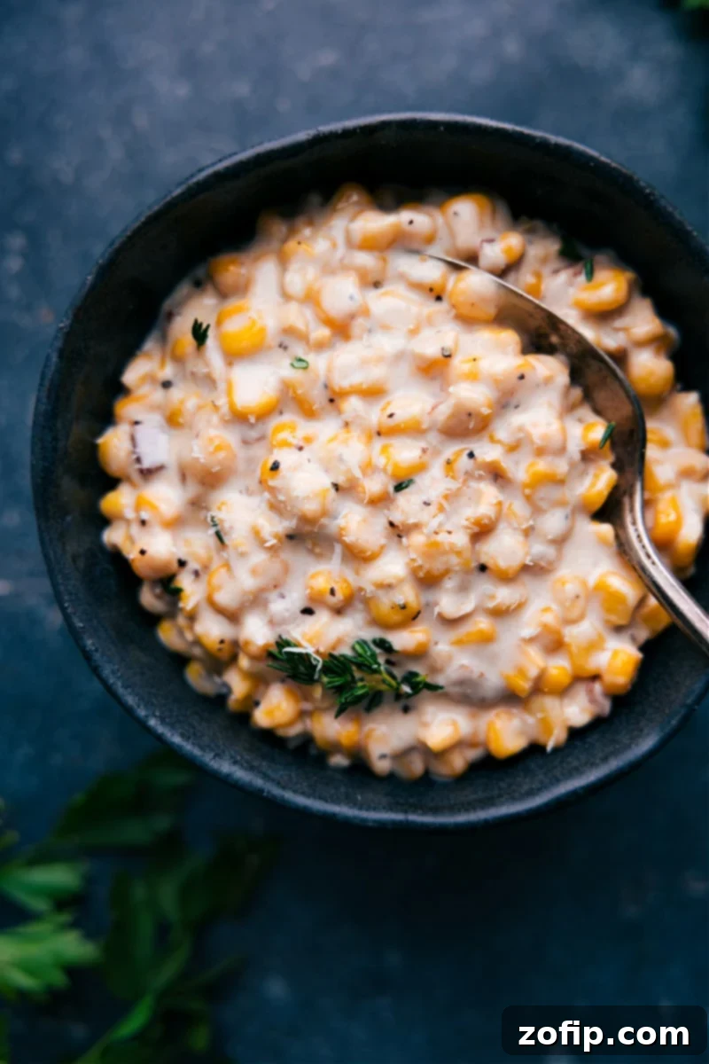 Overhead image of a serving bowl filled with creamy, golden creamed corn, garnished with fresh green herbs