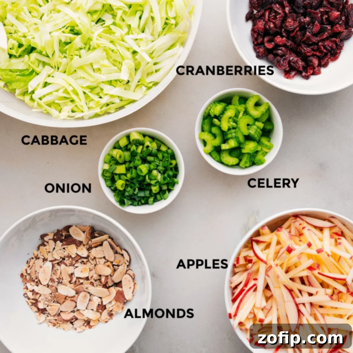 All the fresh ingredients for the apple coleslaw recipe, meticulously prepped and laid out for easy assembly: sliced cabbage, diced apples, cranberries, and almonds.