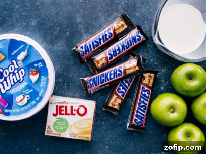 Ingredients for Snickers Salad laid out: Snickers bars, Granny Smith apples, vanilla pudding mix, milk, whipped topping.