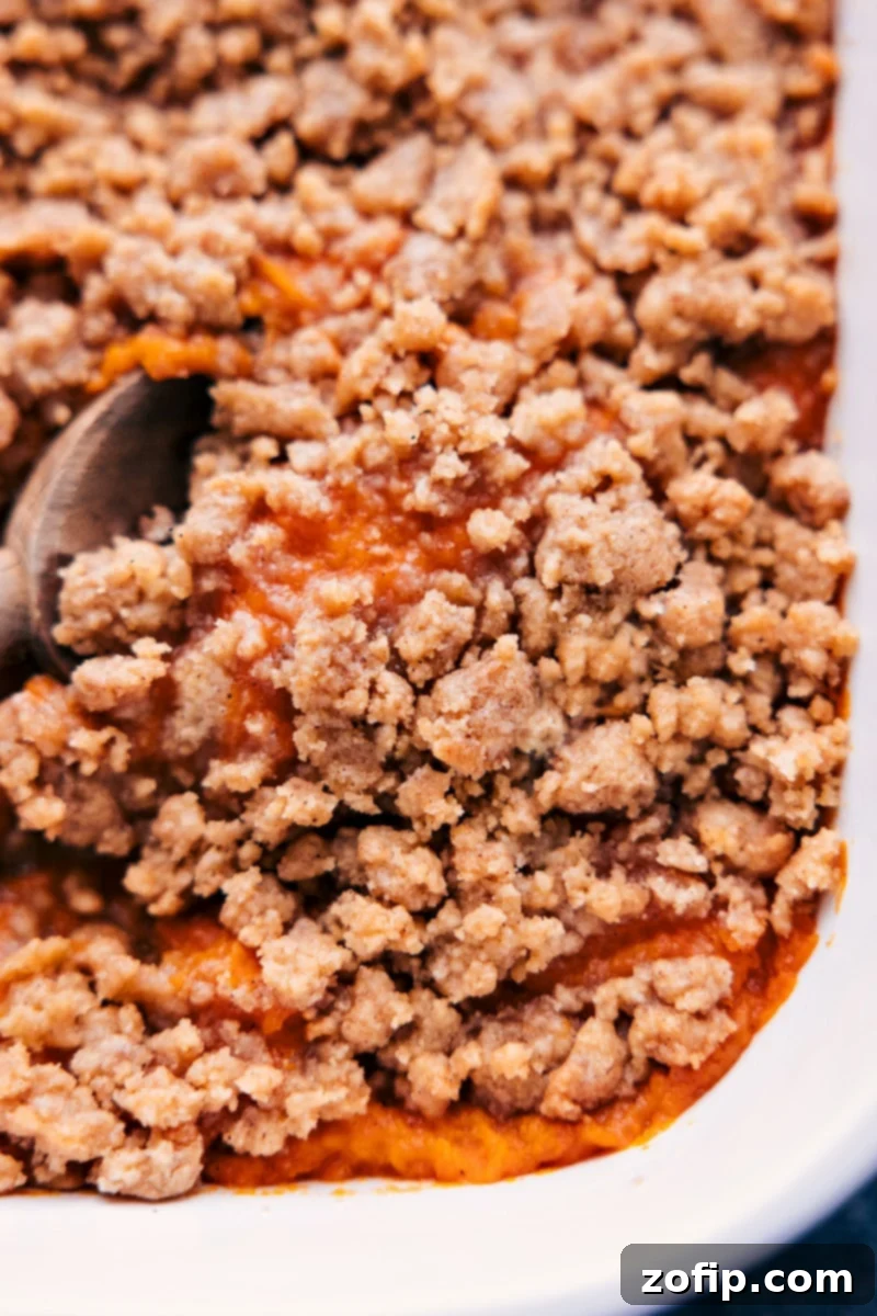 Serving Delicious Sweet Potato Casserole Up-close overhead image of a serving of the sweet potato casserole, revealing its creamy texture and the golden-brown streusel topping, garnished with a sprig of rosemary.