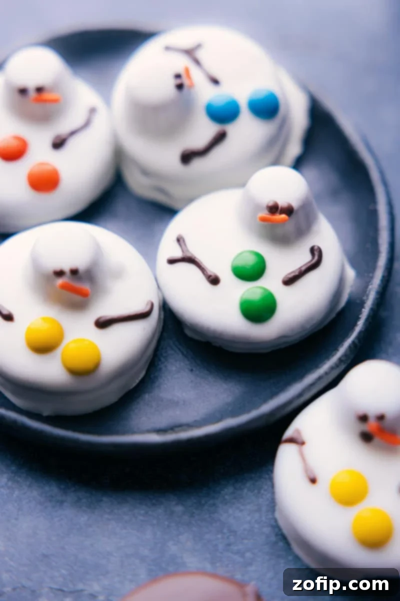Overhead image of a tray of whimsical melted snowman Christmas Oreos, adorned with chocolate arms, button candies, and an orange sprinkle nose.