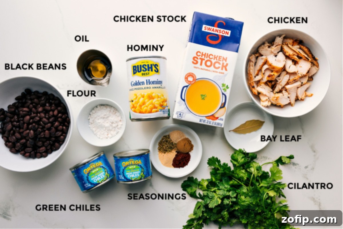 Prepped ingredients for this recipe laid out for easy assembly, including black beans, flour, green chiles, seasonings, oil, hominy, stock, bay leaf, chicken, and cilantro.