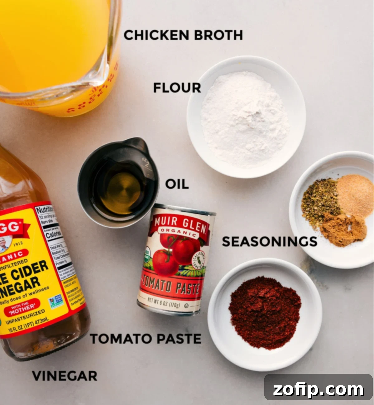 Key Ingredients for Enchilada Sauce All the essential ingredients for a delicious enchilada sauce are neatly laid out: chicken broth, flour, a blend of vibrant seasonings, cooking oil, rich tomato paste, and a touch of apple cider vinegar.