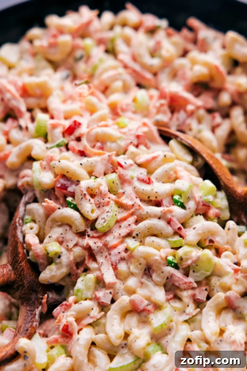 Close-up view of a large bowl of creamy Macaroni Salad, garnished with fresh green onions and parsley, ready to be served.