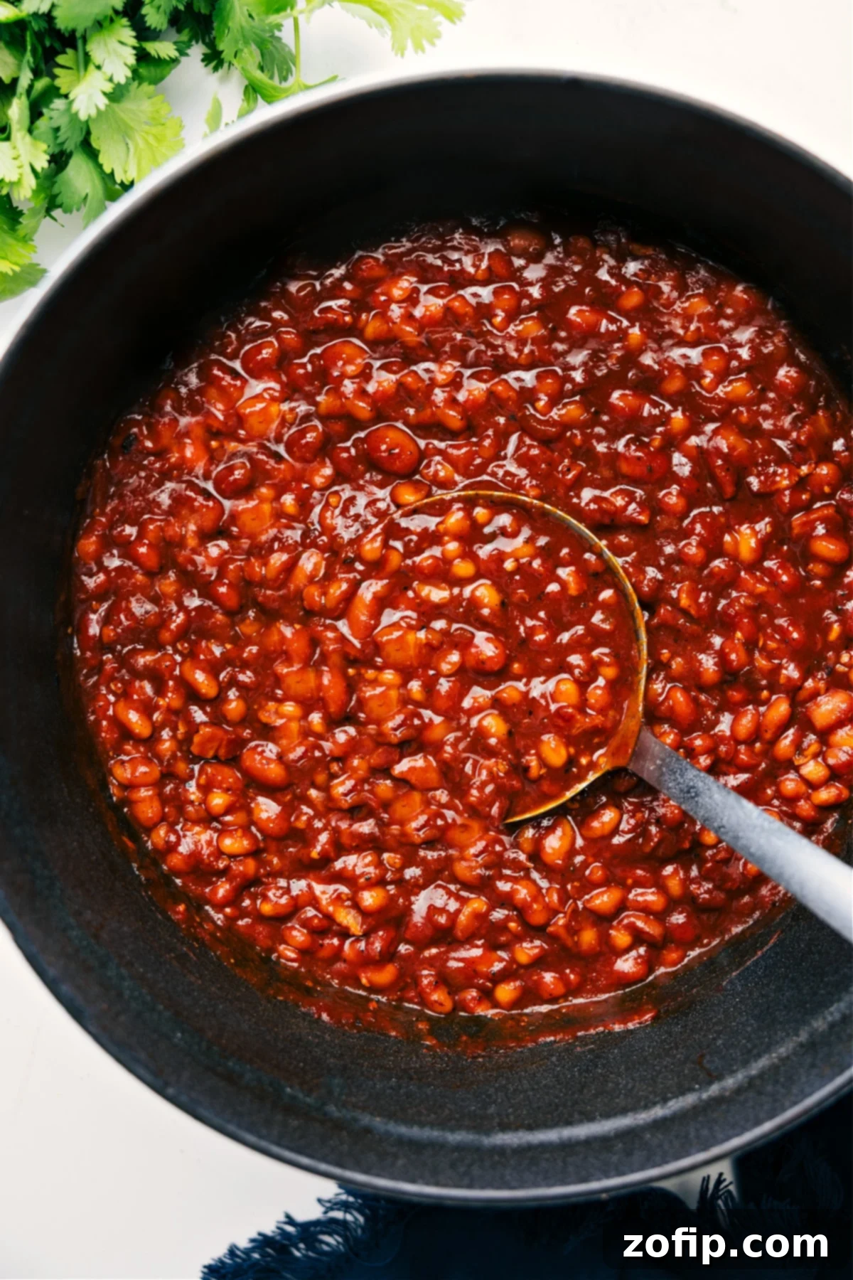 Hearty baked beans simmering in a pot with a wooden ladle lifting a rich, succulent scoop. The beans are glistening with a thick, savory sauce, ready to be served.