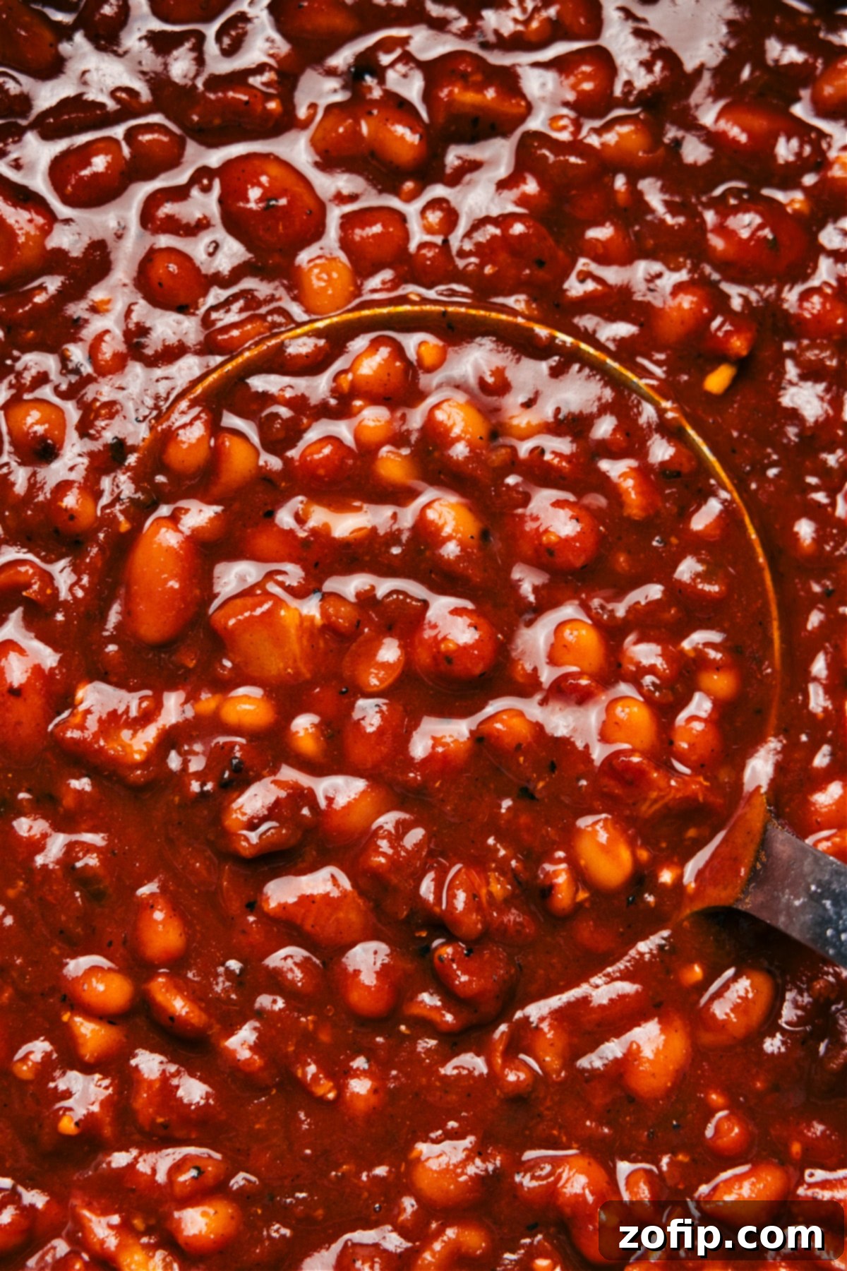 A large cast-iron pot filled with steaming, richly colored baked beans, perfectly cooked and glistening with a thick, savory-sweet sauce, garnished and ready to be served as the ultimate comfort food side dish.