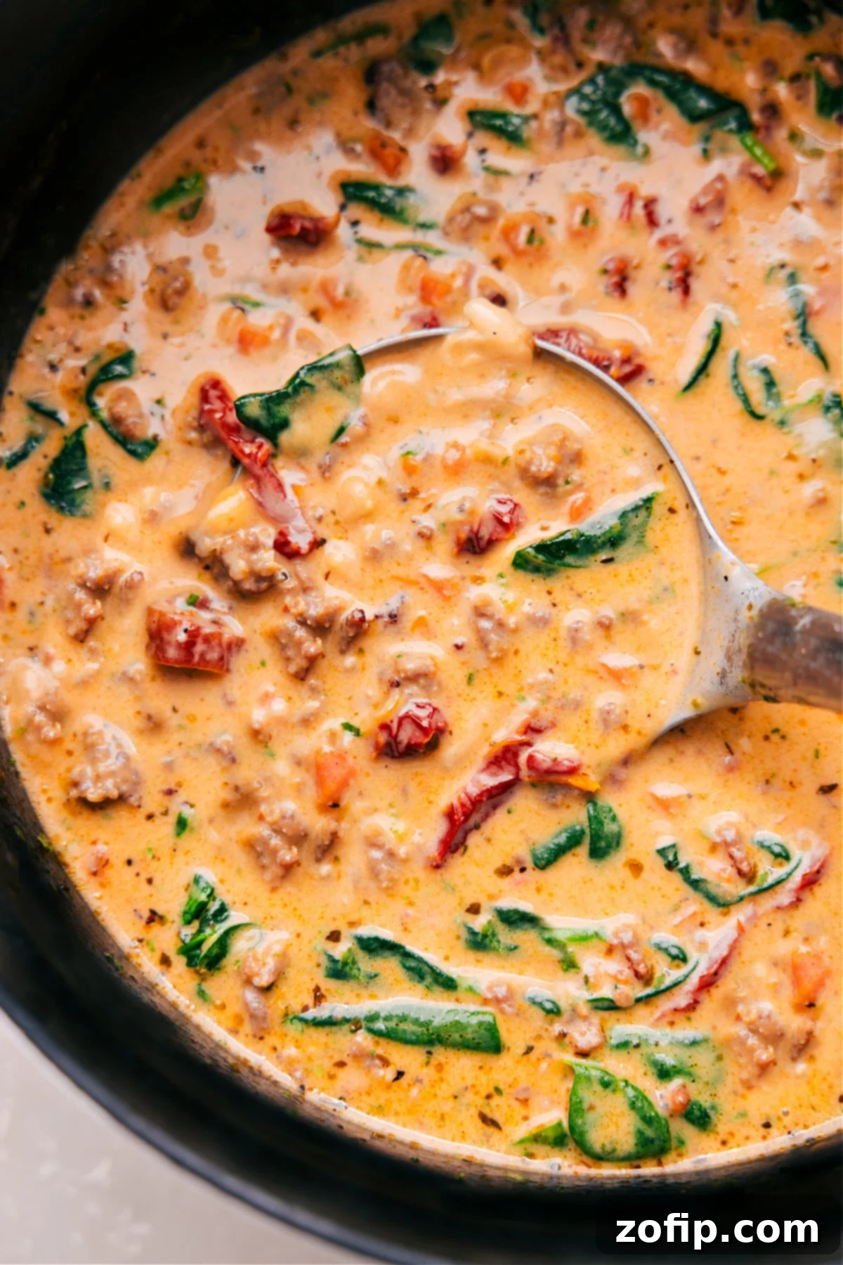 A ladle scooping a rich and creamy Tuscan Soup from a large pot, showcasing the sausage, beans, and spinach.