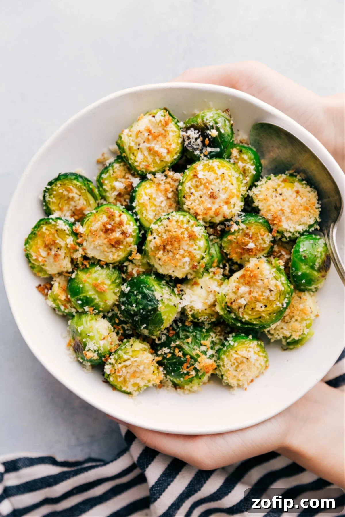 A beautifully presented bowl of golden-brown, perfectly crispy roasted Brussels sprouts, garnished with fresh herbs and a sprinkle of cheese, viewed from directly above.