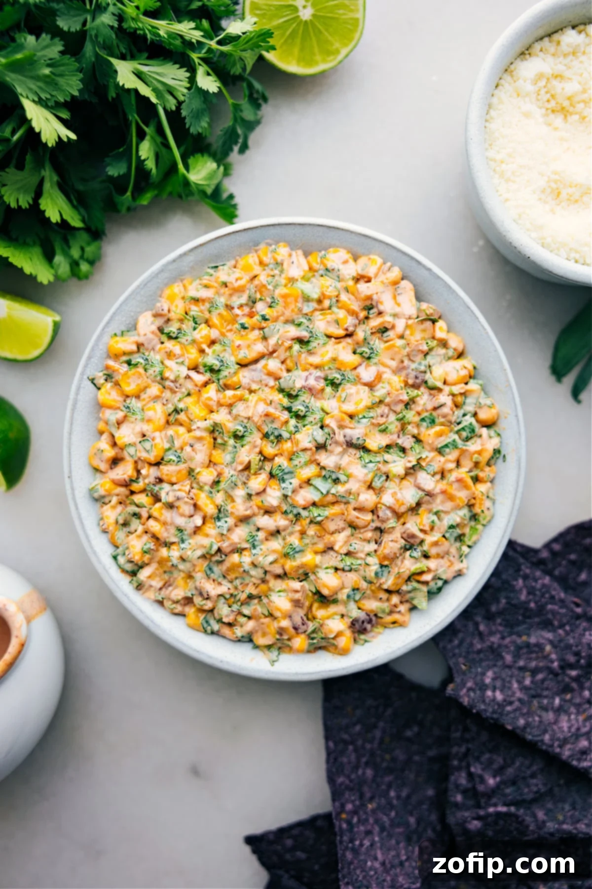 A vibrant bowl of Mexican Street Corn Dip, garnished with fresh cilantro and crumbled Cotija cheese, surrounded by crispy tortilla chips, ready for dipping.