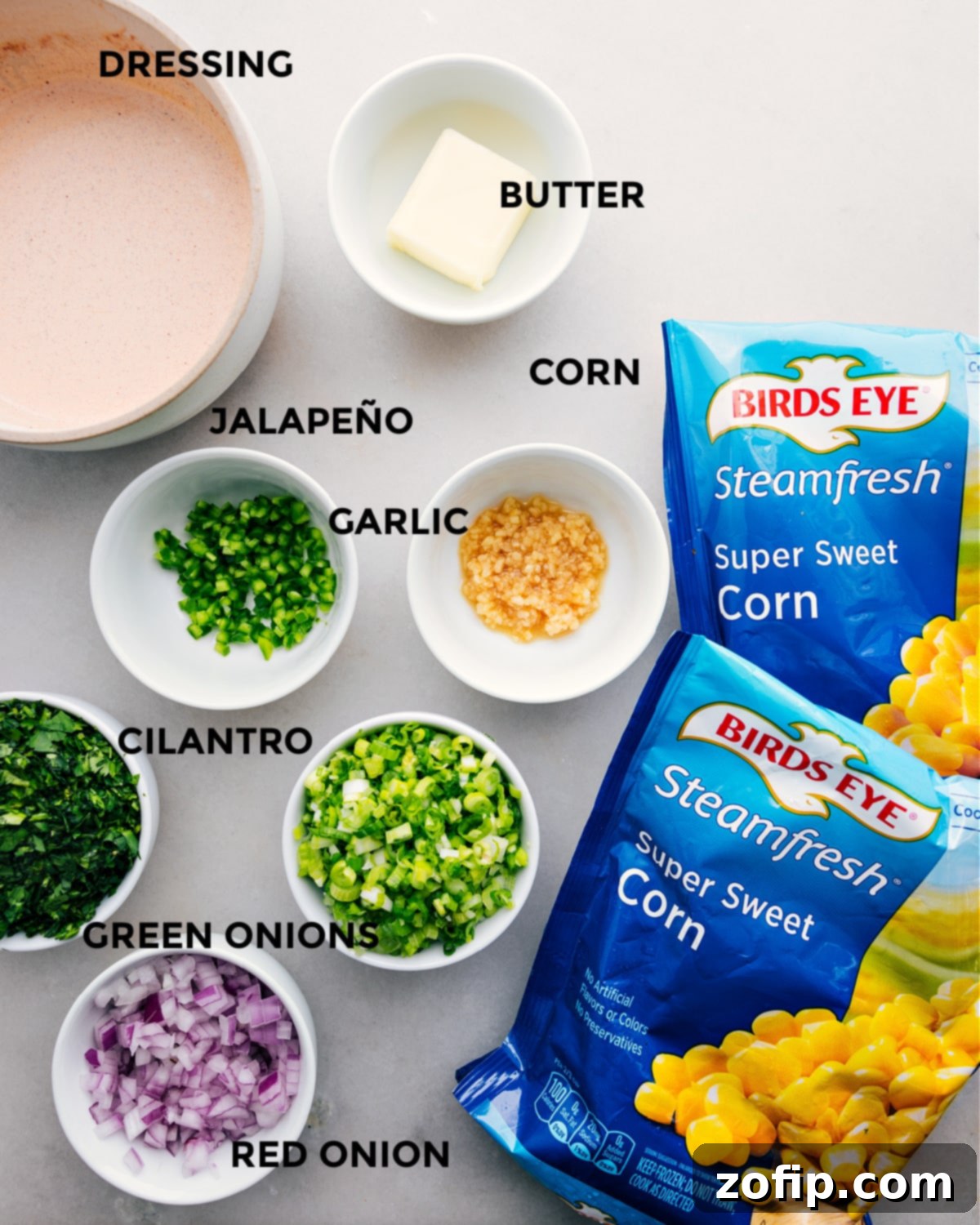 All the fresh ingredients for Mexican Street Corn Dip prepped and laid out on a cutting board, including corn, red onion, jalapeño, cilantro, green onions, and limes, ready for assembly.