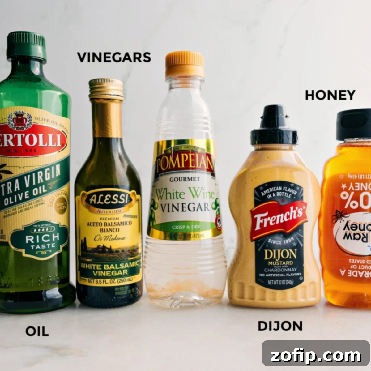 Essential Ingredients for White Balsamic Vinaigrette Recipe Arrangement of White Balsamic Vinaigrette ingredients: a bottle of olive oil, white balsamic vinegar, white wine vinegar, a jar of Dijon mustard, and a small pot of honey, all prepared for mixing.