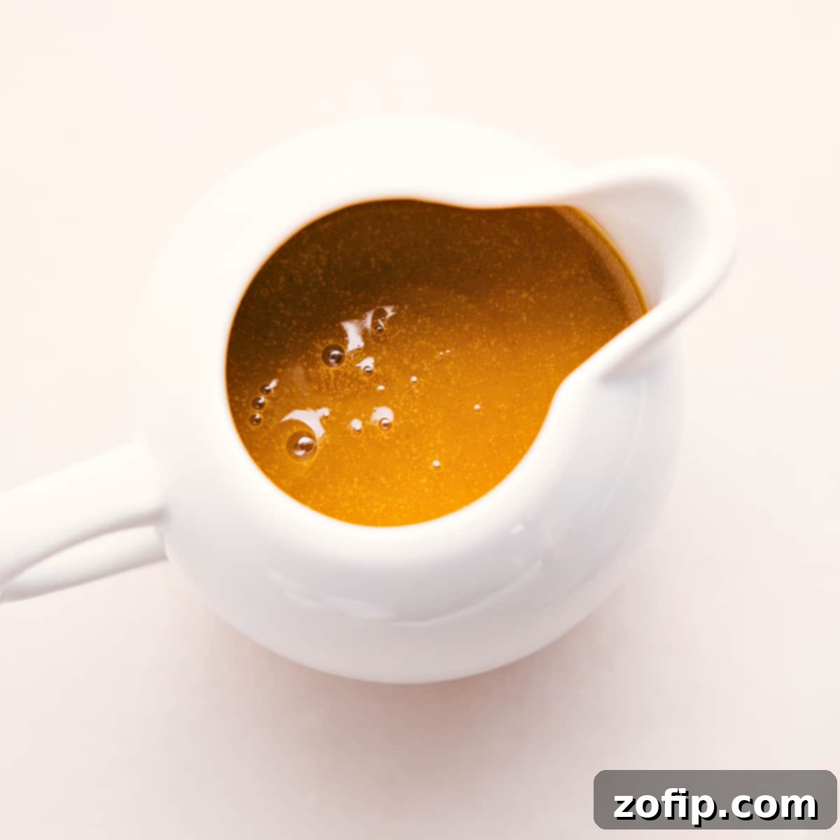 How To Make The Best White Balsamic Vinaigrette A glass dressing jar elegantly filled with smooth White Balsamic Vinaigrette, garnished with a fresh herb sprig, sitting on a wooden surface, ready to be served.