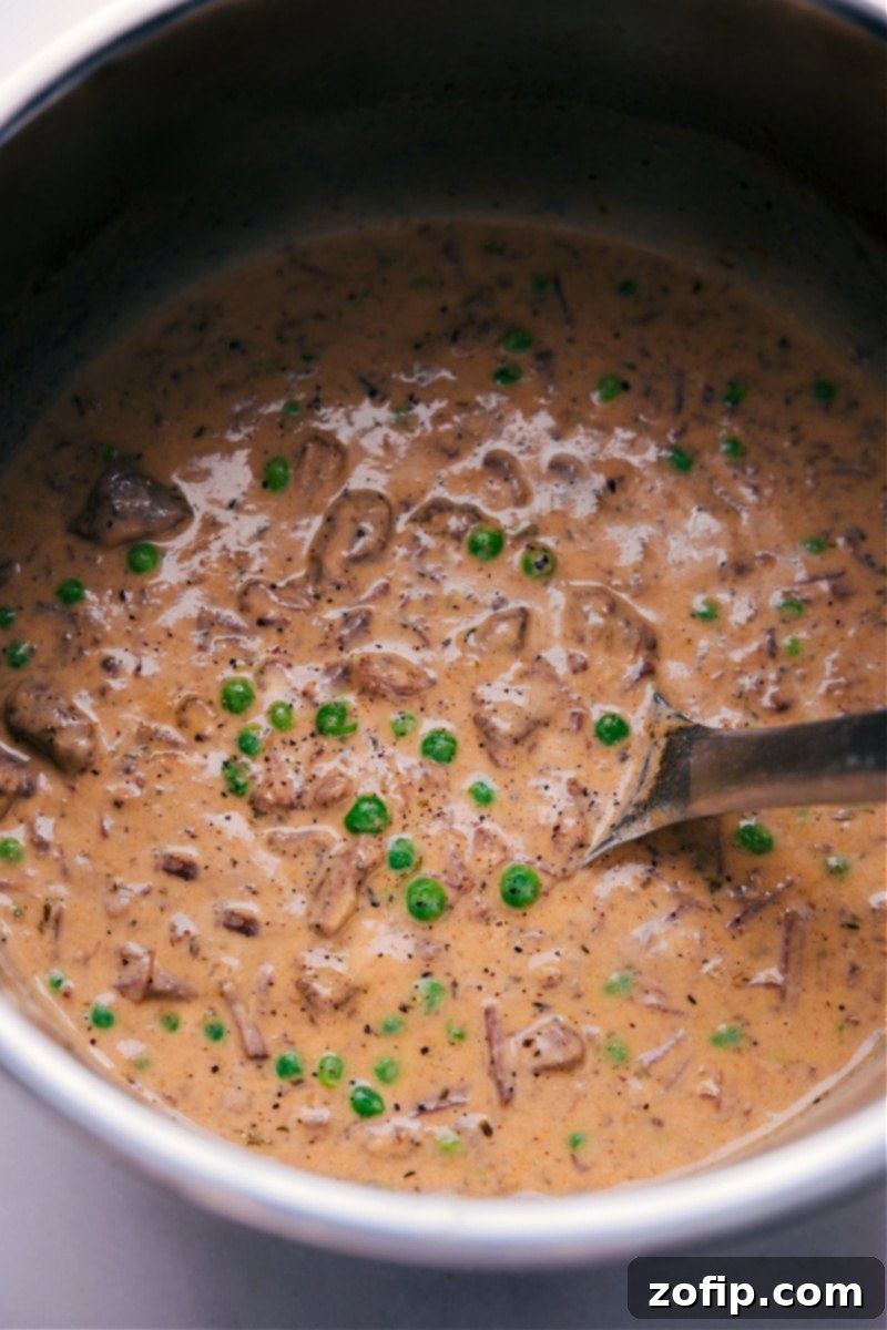 Treat yourself to the ultimate comfort food with this delightful Beef and Noodles recipe. It boasts juicy, tender beef and sweet peas, bathed in a luxuriously rich and flavorful sauce. Enjoy the epitome of coziness, served over egg noodles or mashed potatoes--it's a satisfying meal that you'll crave again and again. Overhead view of the finished Beef and Noodles dish in a bowl