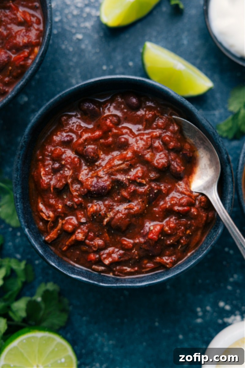 Overhead image of a bowl of Chili Con Carne ready to be enjoyed, garnished with shredded cheese and a dollop of sour cream.