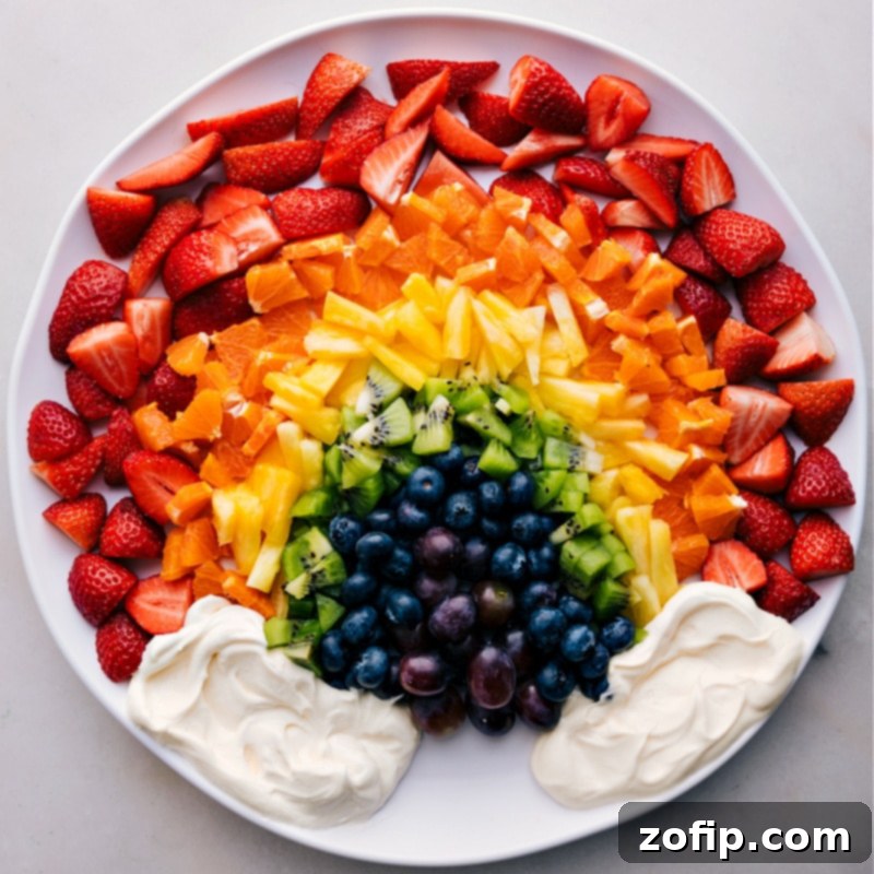 An inviting overhead view of the complete Rainbow Fruit Tray, meticulously arranged with a vibrant variety of colorful fresh fruits and a central bowl of creamy white fruit dip, presented beautifully on a platter, ready to be served and enjoyed at a gathering.