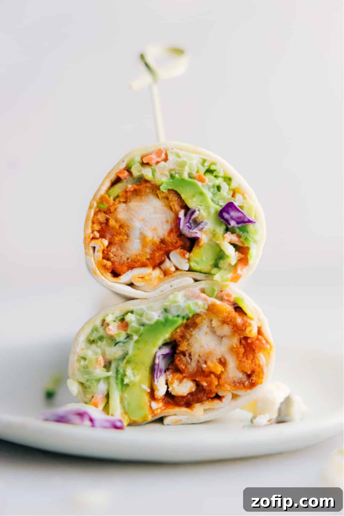Two Buffalo Chicken Wraps, cut in half and stacked, revealing the layers of crispy buffalo chicken, vibrant slaw, and creamy dressing inside.