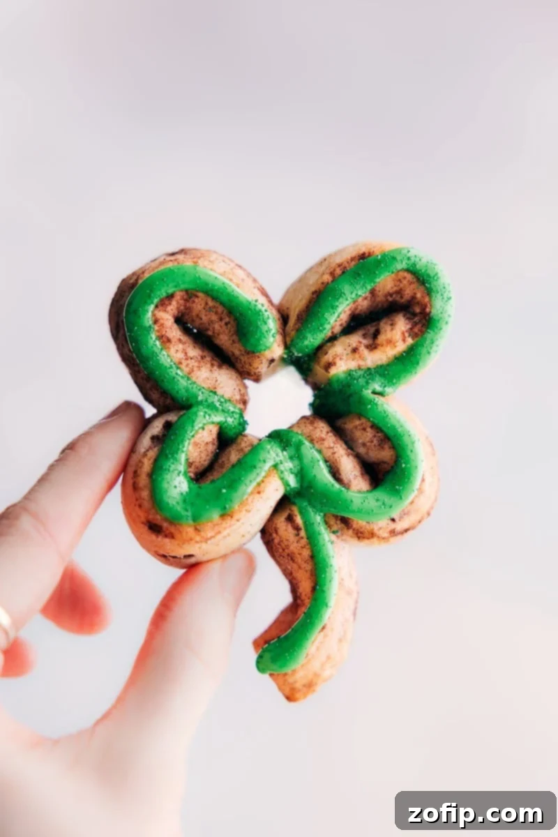 Delicious Shamrock Cinnamon Roll with green icing, perfect for St. Patrick's Day celebrations. A freshly baked Shamrock Cinnamon Roll, perfectly glazed with green icing and held up to show its festive shape, ready to be enjoyed on St. Patrick's Day.
