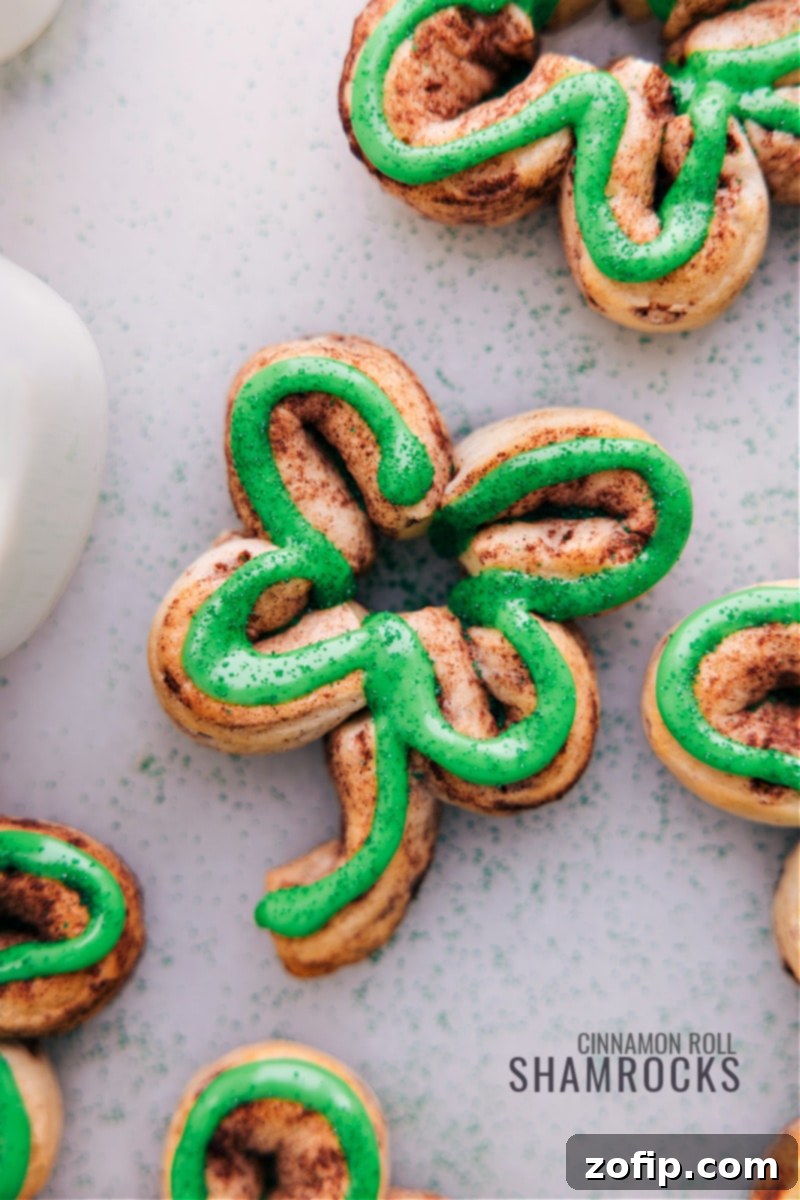 A plate of delicious Shamrock Cinnamon Rolls, iced and ready for St. Patrick's Day. Overhead close-up view of several beautifully iced Shamrock Cinnamon Rolls, arranged on a plate, showcasing their vibrant green frosting and charming clover shape, ready to be served.