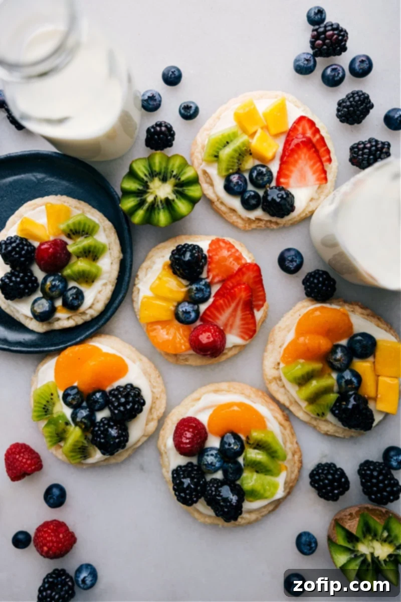 Overhead view of several vibrant Sugar Cookie Fruit Pizzas arranged artfully on a serving platter, showcasing colorful fresh berries and a glossy glaze.