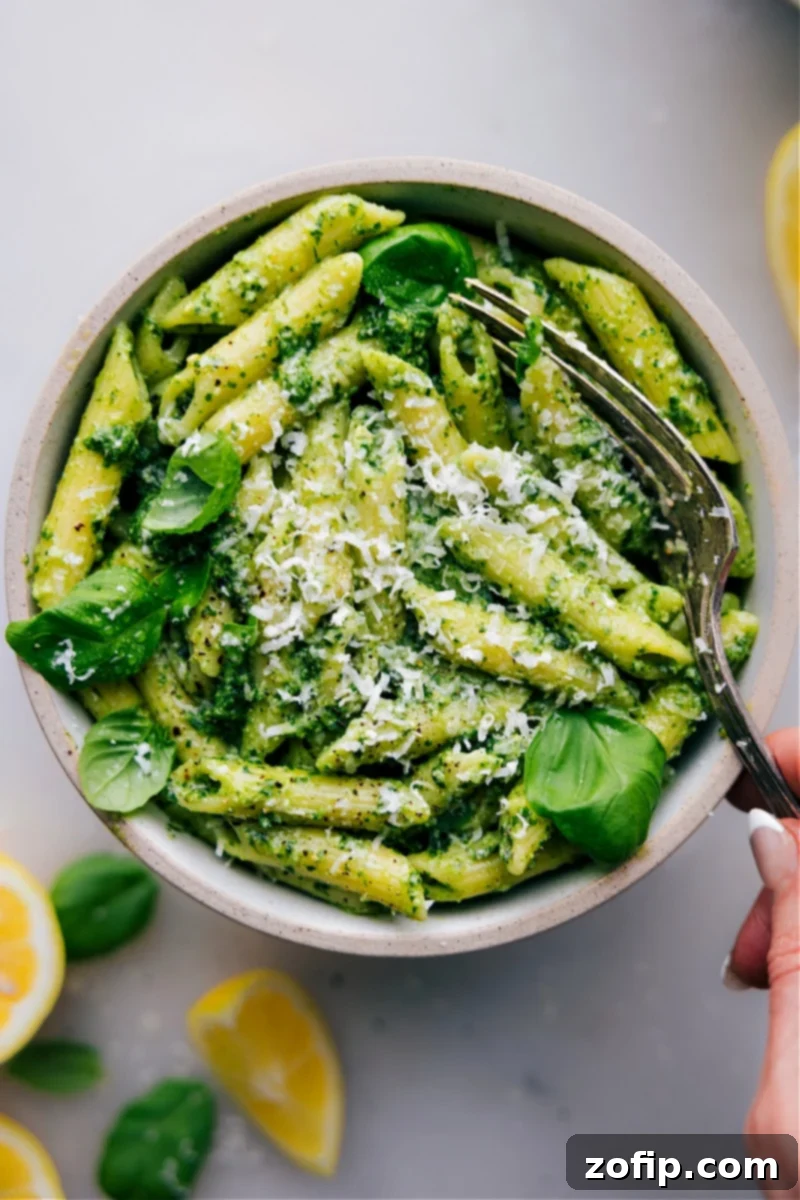 Overhead image of vibrant green Pesto Pasta in a bowl, garnished with fresh basil and Parmesan cheese.