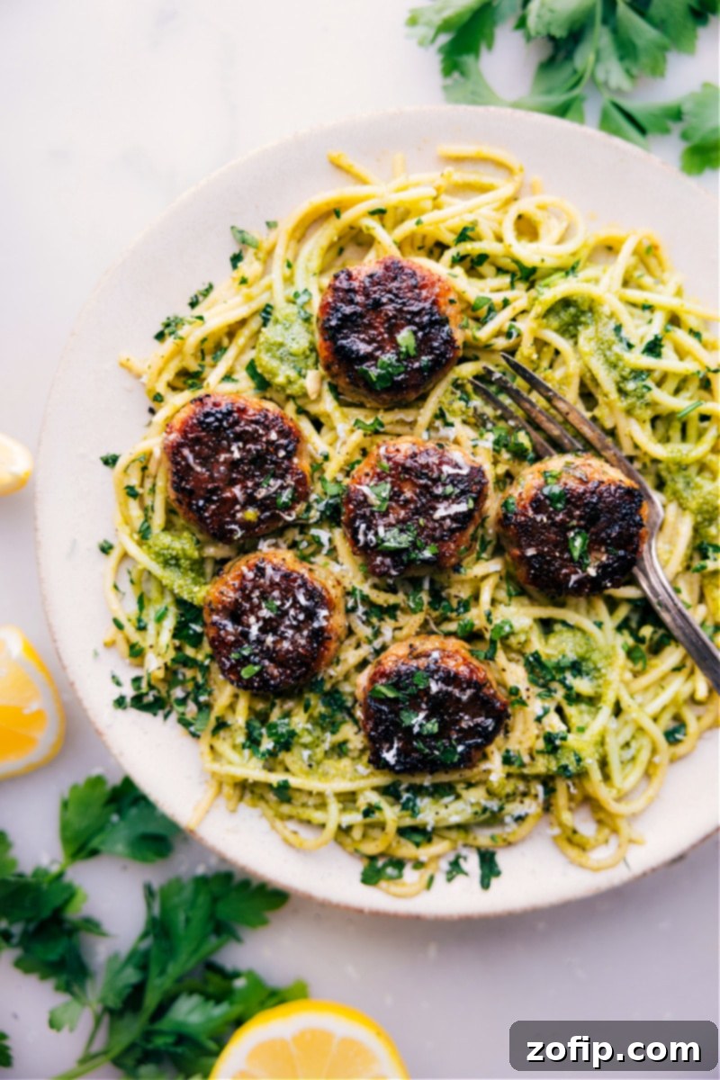 Hearty and delicious chicken meatballs served atop a generous portion of pesto pasta. A perfectly plated dish of chicken meatballs resting on a bed of vibrant green pesto pasta, garnished with fresh basil leaves and parmesan, ready to eat.