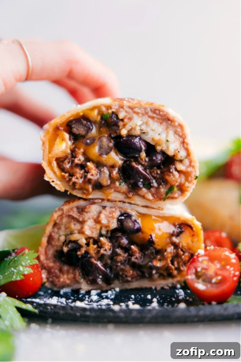 Two halves of a delicious, hearty beef burrito stacked, showing layers of seasoned ground beef, cilantro lime rice, refried beans, and melted cheese