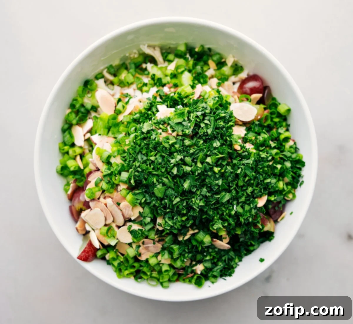 All the vibrant ingredients for the healthy chicken salad being added to a large bowl, ready to be tossed together with the creamy dressing.