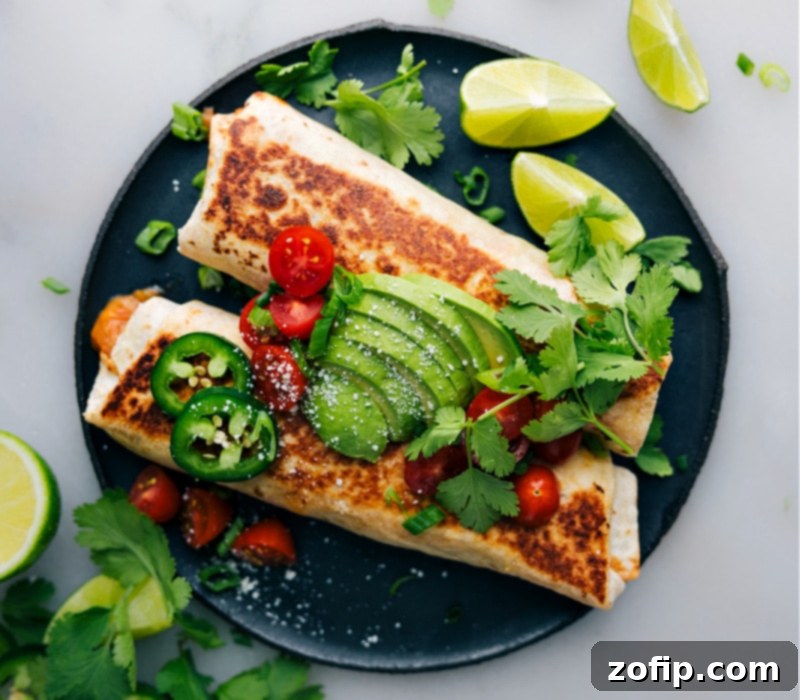 An overhead shot of two perfectly baked bean and cheese burritos, garnished with fresh toppings like avocado, pico de gallo, and sour cream, ready to eat.