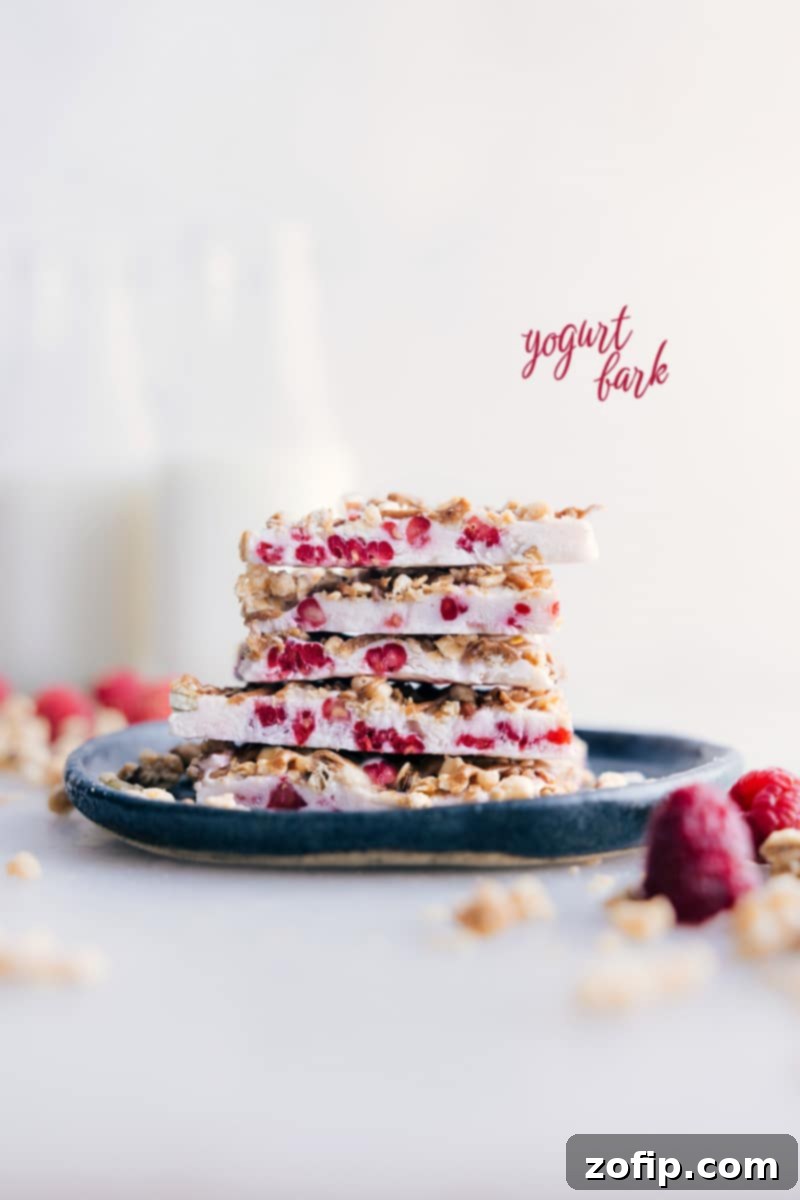 Stacked pieces of raspberry Greek yogurt bark with pistachios and granola, ready to eat.