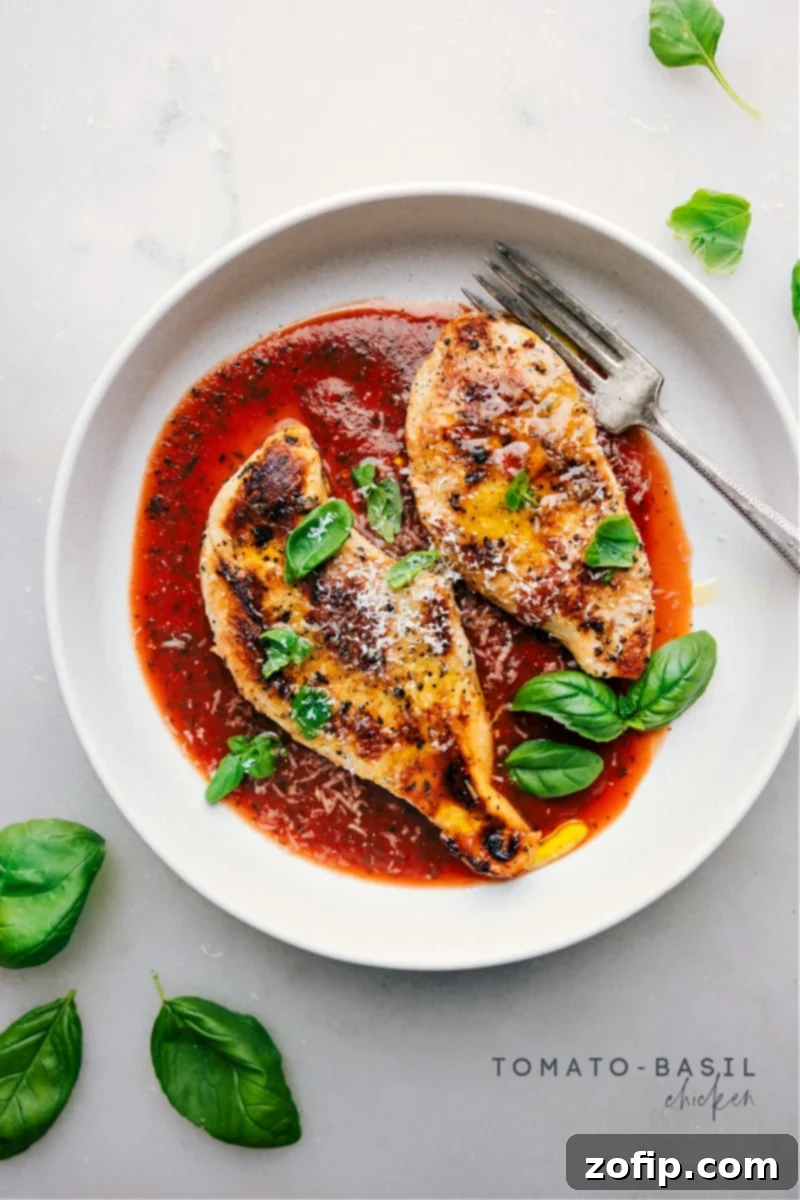 Overhead image of freshly cooked Tomato-Basil Chicken in a skillet, garnished with fresh basil leaves and shaved Parmesan.