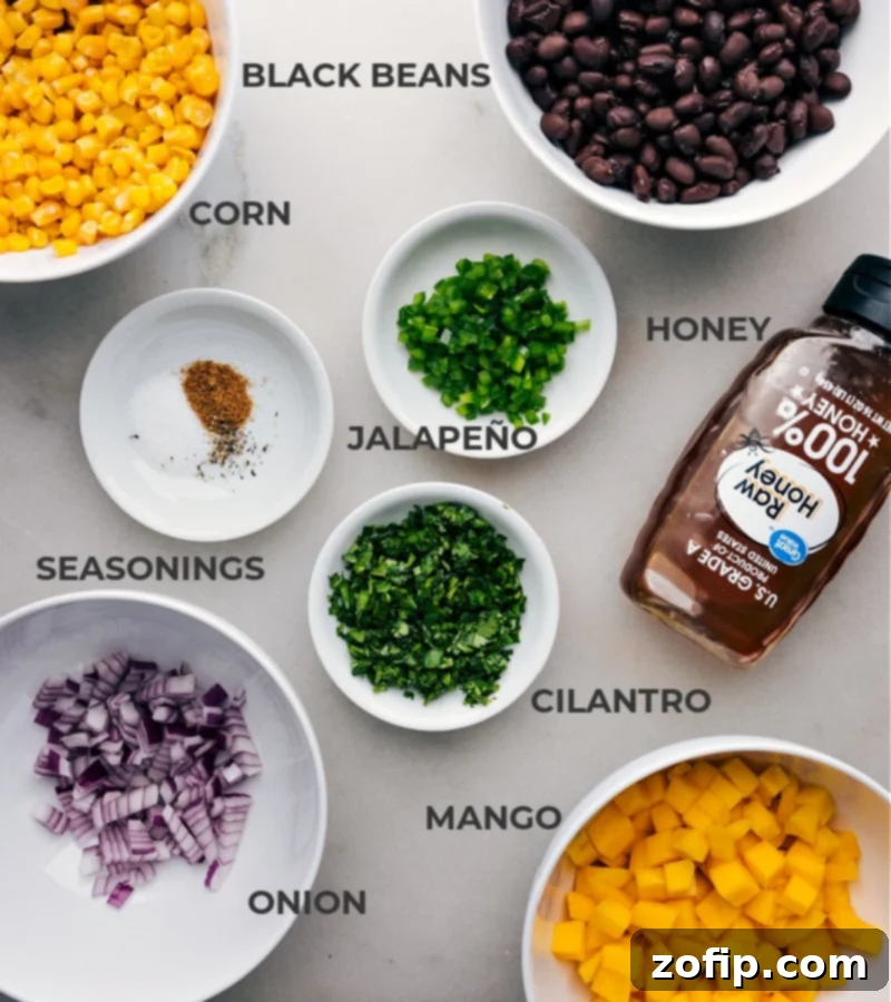 Ingredients In Mango Black Bean Salsa All the fresh ingredients for Mango Black Bean Salsa laid out on a cutting board, including vibrant diced mango, black beans, corn kernels, chopped red onion, fresh cilantro, sliced jalapeño, whole lime, honey, olive oil, and a selection of spices.