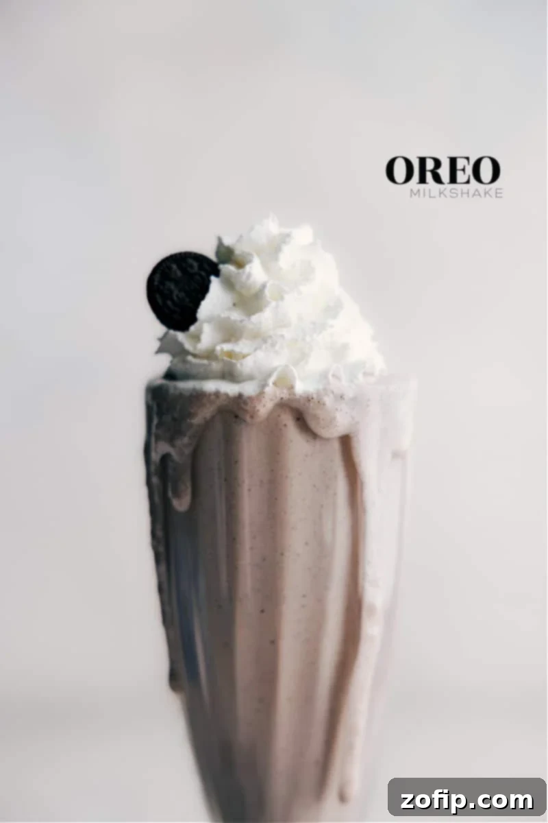 The Ultimate Thick and Creamy Oreo Milkshake, made with cookies and cream ice cream, vanilla, and a hint of salt. A tall glass of the ultimate Oreo Milkshake, garnished with whipped cream and crushed cookie bits, inviting you to take a sip.