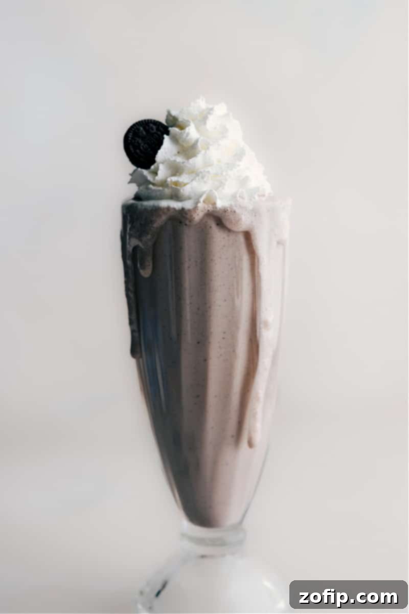 Our favorite Oreo Milkshake, perfectly blended and ready to be enjoyed. A person holding a glass of the delicious Oreo Milkshake, ready to take the first sip. The shake is topped with whipped cream and crushed cookies, looking perfectly refreshing and inviting.