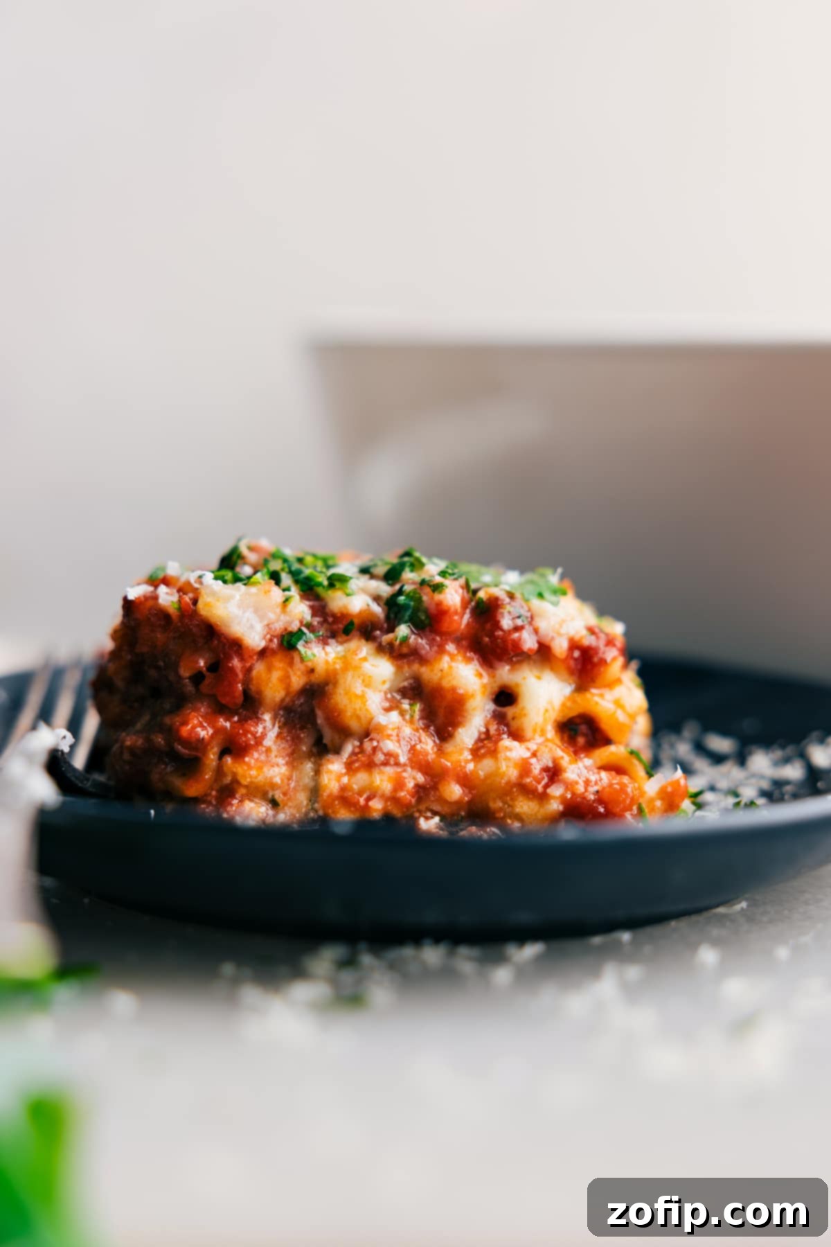 Steaming slice of Lasagna layered with cheese and sauce on a plate, ready to eat.