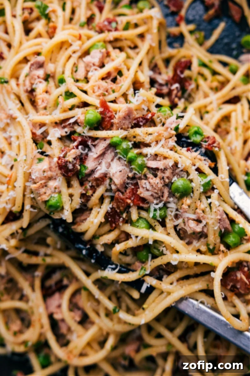 Delicious Healthy Tuna Pasta Ready to Serve A vibrant bowl of healthy tuna pasta, garnished with fresh parsley and grated Parmesan cheese, ready to be enjoyed. The pasta is perfectly coated in a light sauce with visible chunks of tuna and sun-dried tomatoes.