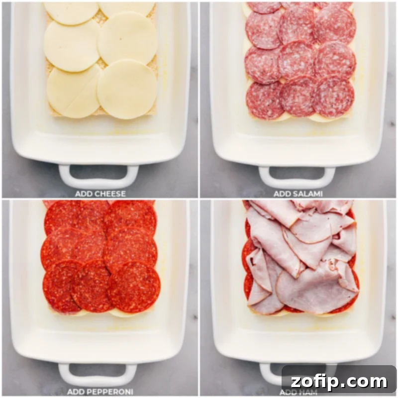 Layers of creamy Provolone cheese, savory salami, zesty pepperoni, and tender ham arranged neatly on the bottom half of sweet Hawaiian rolls in a baking dish, ready for the top layer.