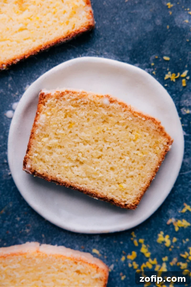 The ultimate Iced Lemon Bread recipe: supremely moist with bright citrus flavor, a perfect pound-cake denseness, and ultra-soft thanks to yogurt. A must-try quick bread for breakfast or brunch! Overhead image of a slice of Iced Lemon Bread on a plate, showcasing its moist texture and shiny glaze.