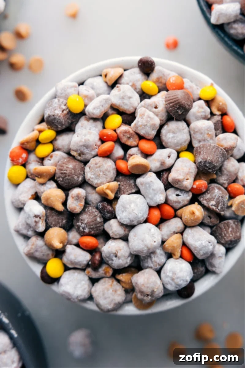 Delicious Peanut Butter Puppy Chow, perfectly coated and ready to enjoy, showcasing its crunchy texture and tempting mix-ins. A close-up, overhead shot of the finished Peanut Butter Puppy Chow with Reese's minis and peanut butter chips, ready to be served and enjoyed.
